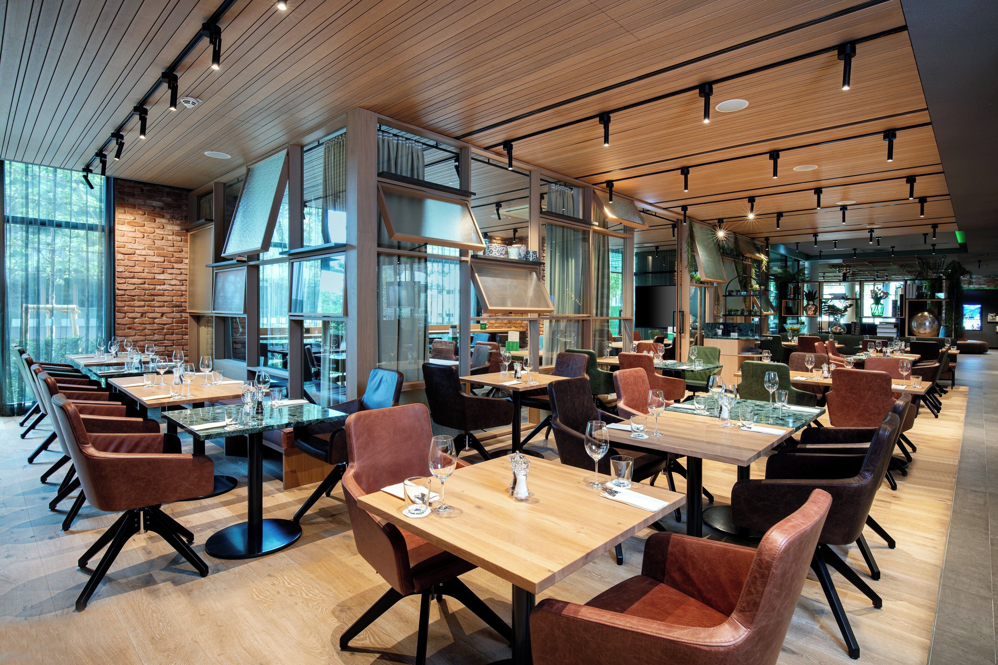 Un restaurante espacioso con varias mesas y sillas, ventanas amplias y techo de madera.
