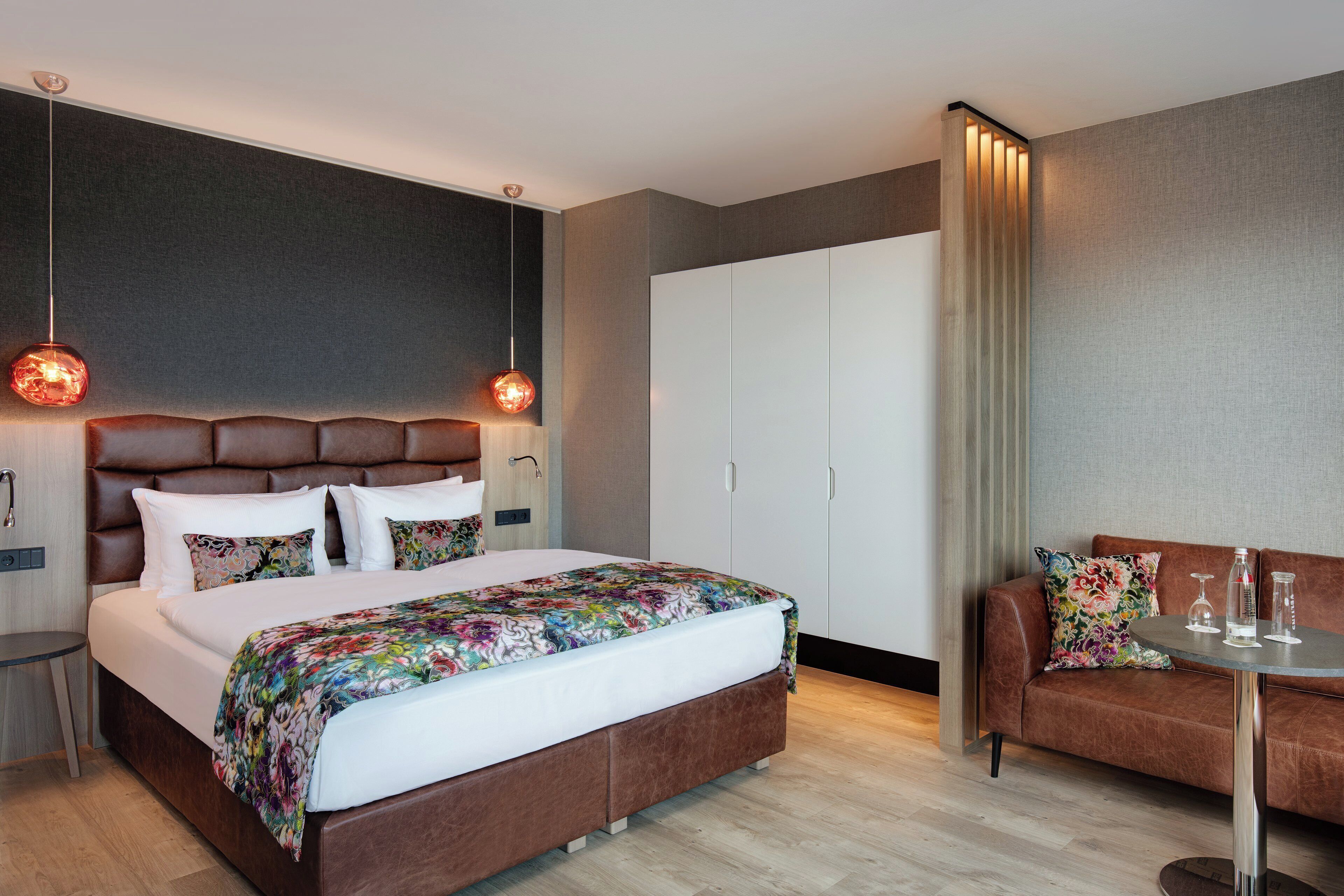 A modern hotel room with a large bed, a sofa, a small table, and a wardrobe.
