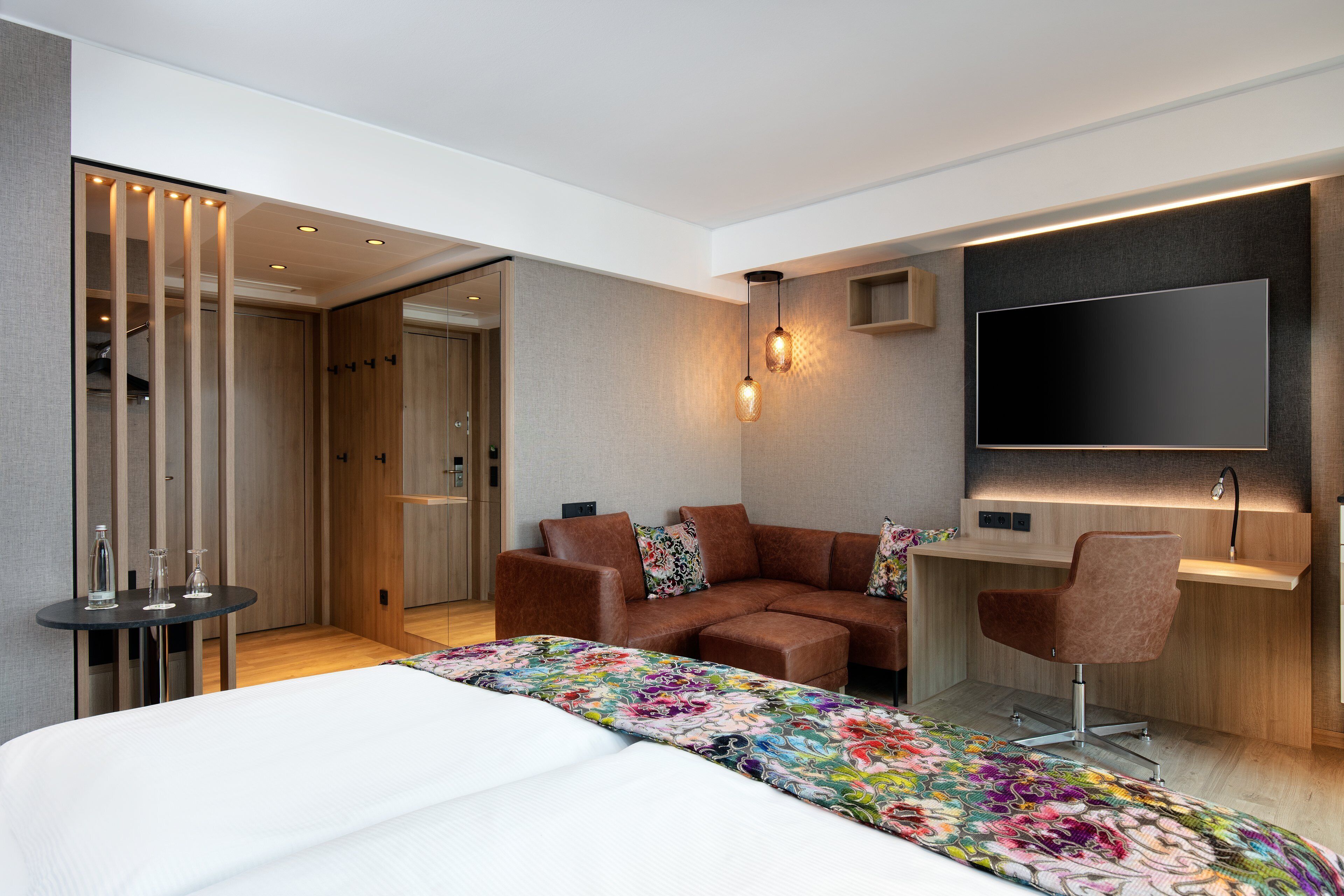 A modern hotel room with a large bed, a sofa, a desk, and a TV.