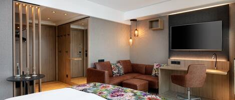 A modern hotel room with a large bed, a sofa, a desk, and a TV.