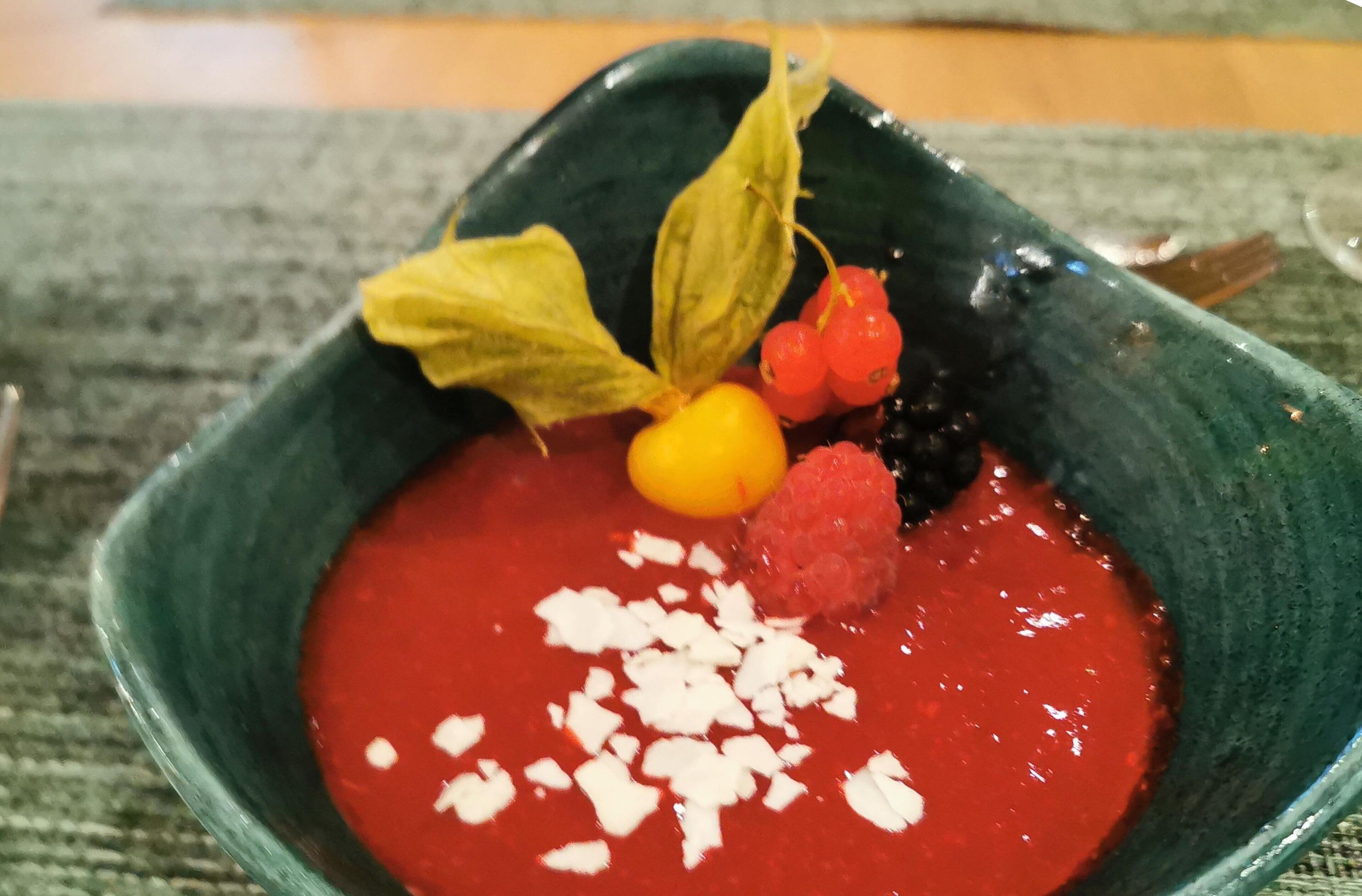 Un postre en un tazón verde con salsa roja, decorado con trozos blancos, bayas y hojas.