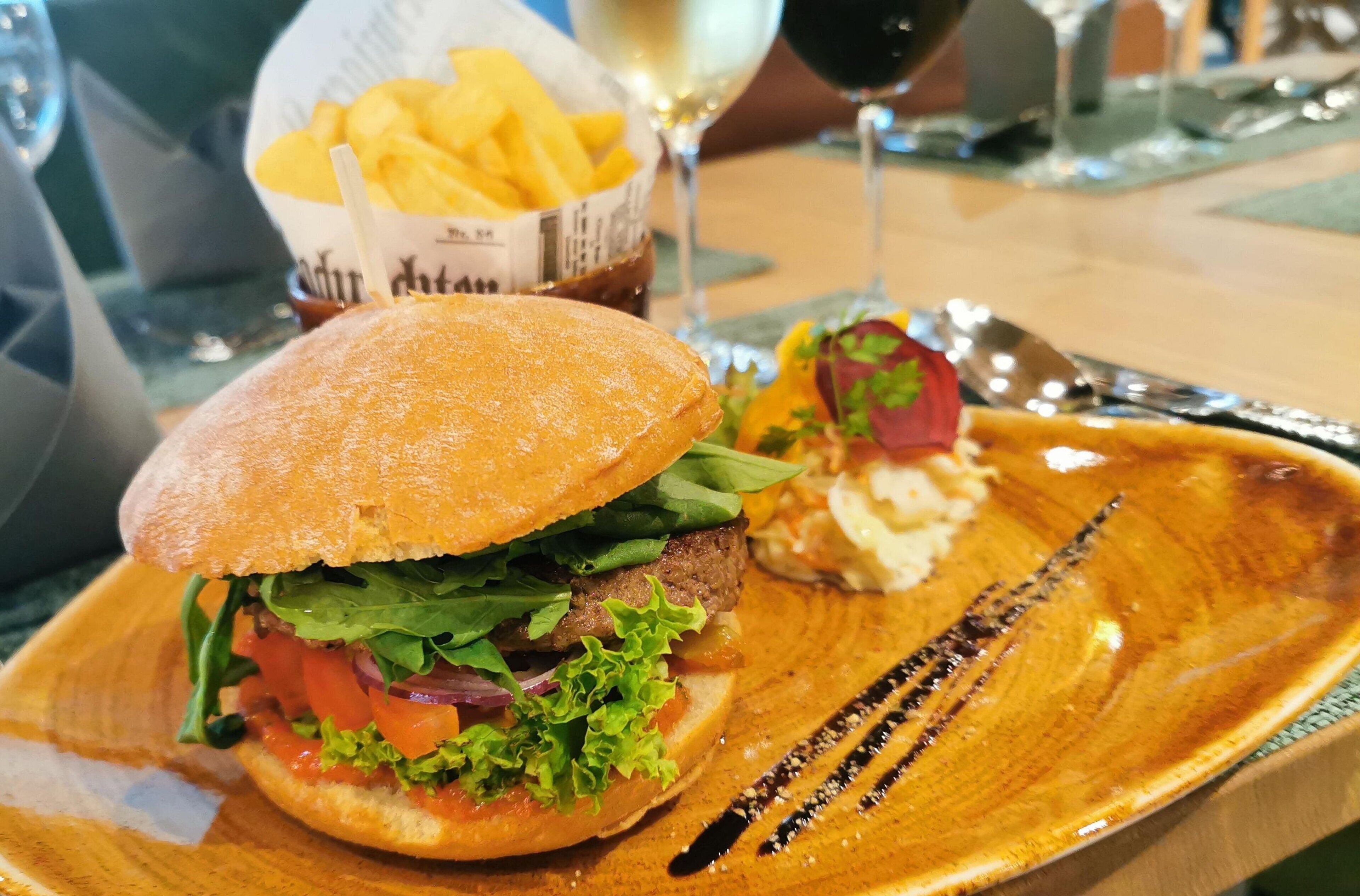 A sandwich on a plate with fries and a drink in the background.