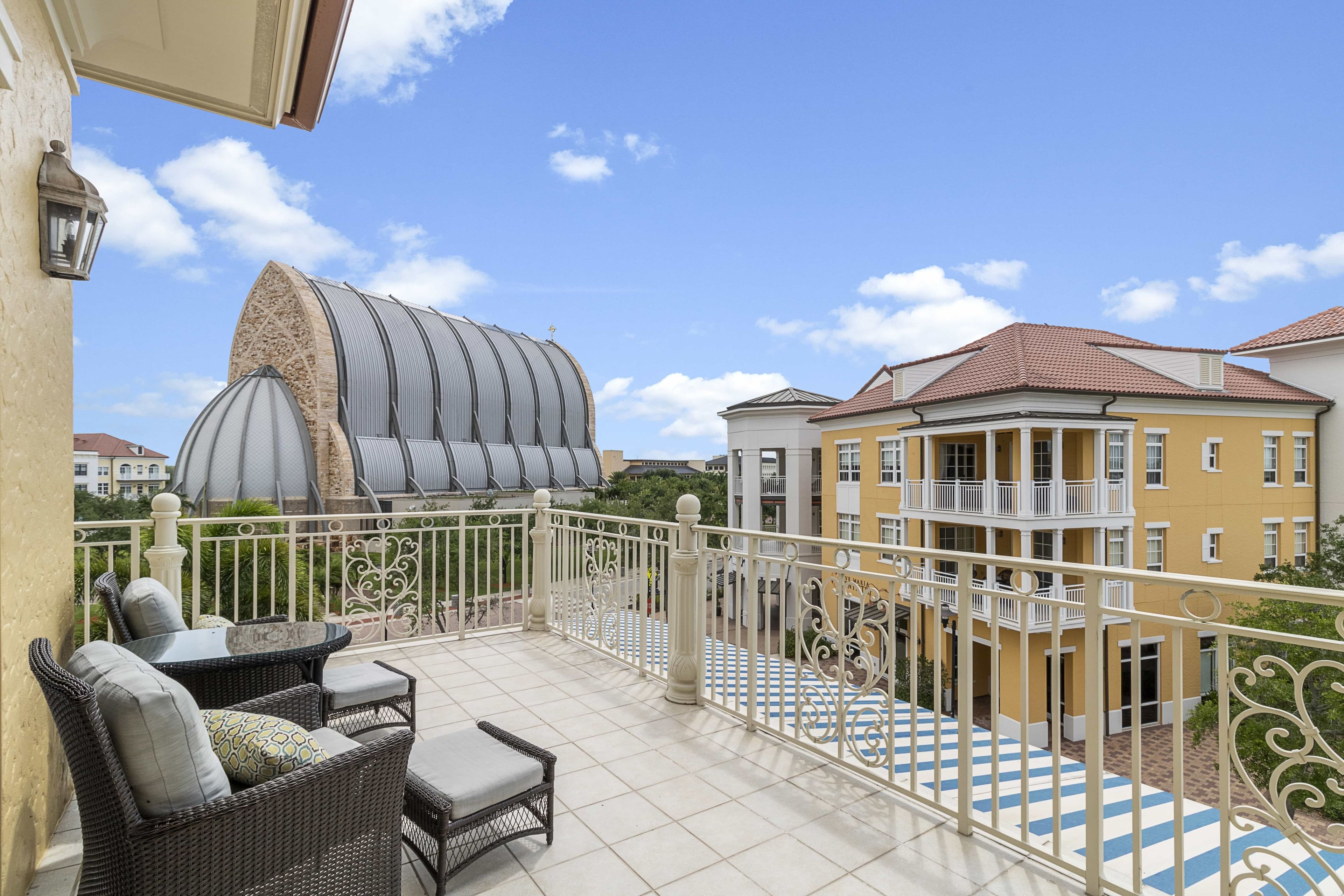 A balcony with wicker furniture, a decorative metal fence, and a view of surrounding buildings.