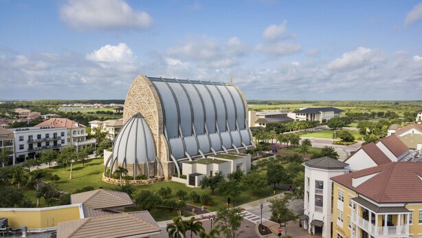 Un edificio moderno con un tetto curvo particolare e una cupola centrale, immerso in zone residenziali e aree verdi.