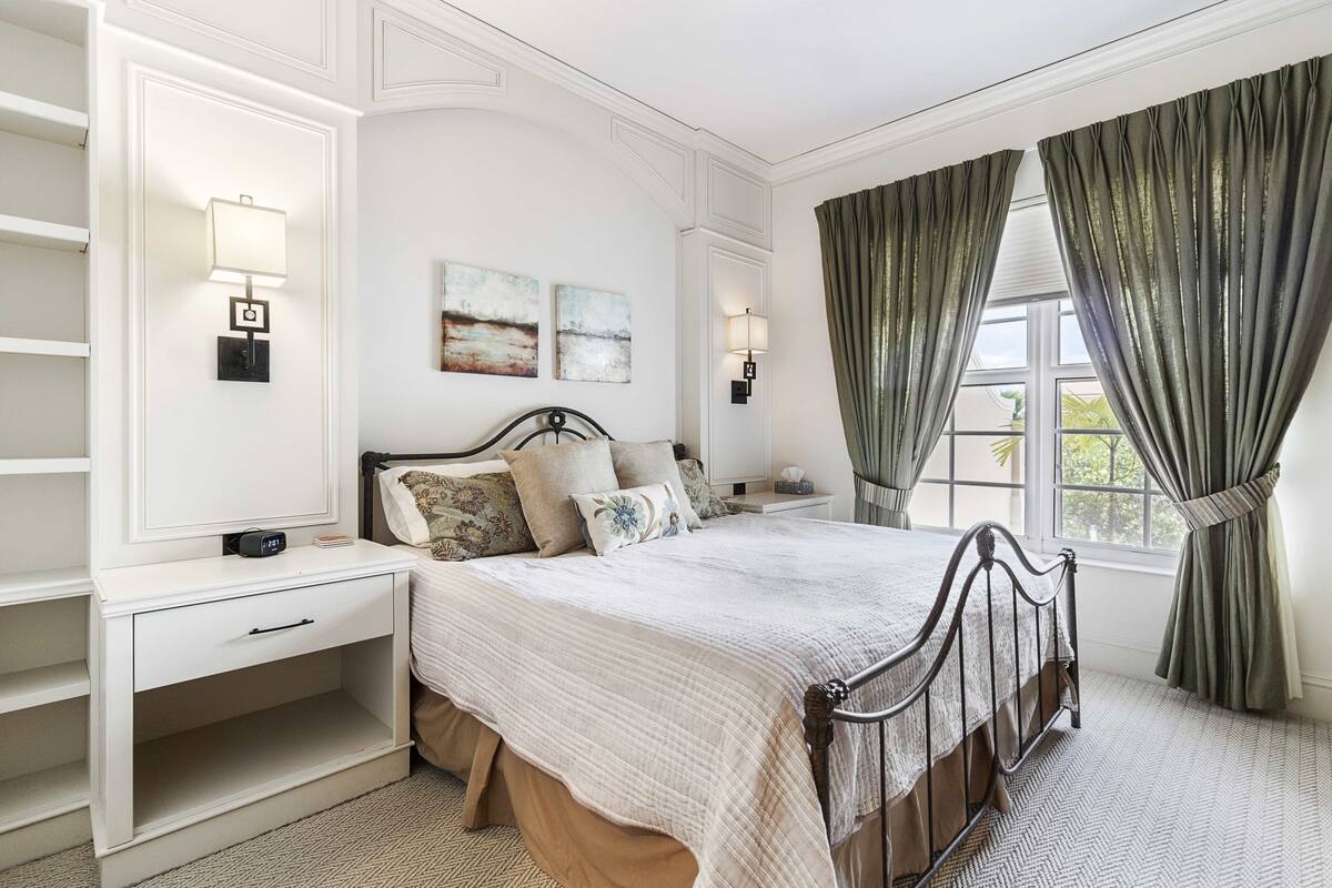 A bedroom with a bed, bedside tables, a nightstand, a lamp, and a window with curtains.