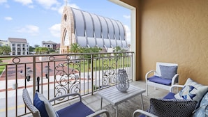 Un balcone con mobili in vimini, vista su un edificio con un tetto caratteristico e cielo sereno.