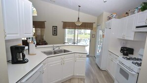 A kitchen with white cabinets, a stove, a sink, and a coffee maker.