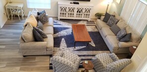 Sala de estar com dois sofás, uma mesa de centro, almofadas estampadas, um armário branco e uma área de jantar com mesa e cadeiras.