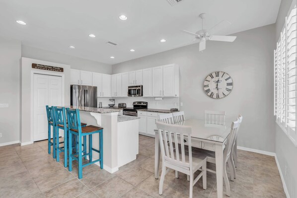 A modern kitchen with white cabinets, a central island, and blue chairs.