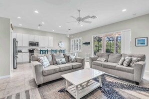 A modern living room with two sofas, a coffee table, and a kitchen in the background. - Pool Home in Spanish Wells with Public Golf (Bonita Springs)
