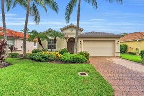 A residential house with a garage, a well-maintained lawn, and palm trees. - Pool Home in Spanish Wells with Public Golf (Bonita Springs)