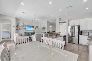 A modern kitchen with white cabinets, a stainless steel refrigerator, and a dining area with a white table and chairs.