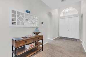 A hallway with a wooden console table, a decorative wall piece, and a white door with a doormat.