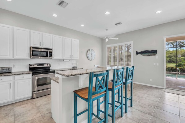 A modern kitchen with white cabinets, stainless steel appliances, a granite countertop, and a bar area with blue chairs.