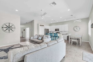 A spacious living area with a large sofa, a dining table with chairs, and a kitchen in the background.