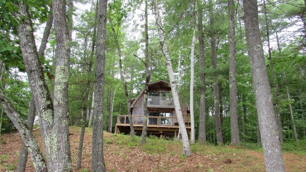 Una cabaña en un bosque con una terraza de madera y un balcón.