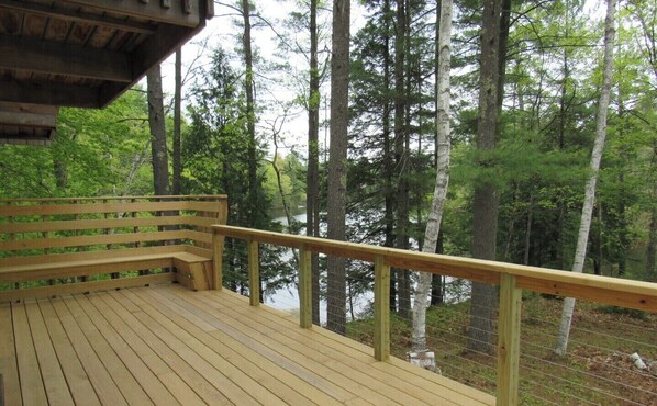 Enjoy a serene view of the forest and water from this deck with a bench and railing.