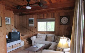 L’intérieur d’un chalet en bois, avec un canapé, une table basse, un téléviseur et une horloge au mur.