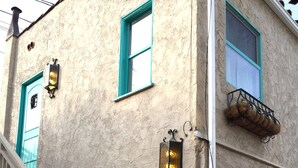 Un edificio con una escalera, una puerta de garaje y dos ventanas con marcos color aguamarina.