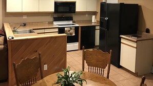 A compact kitchen with a dining area, featuring a microwave, stove, refrigerator, and a potted plant on the table. - Relaxation in the mountains. Hike, Ski & explore around Jay Peak (Lowell)