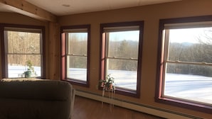A room with three large windows, wooden floors, and a couch. - Relaxation in the mountains. Hike, Ski & explore around Jay Peak (Lowell)