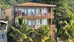 A two-story building with balconies, surrounded by palm trees and a stone wall. - Oceanfront!  Diving, Snorkeling, Kayaking.  Turtle Casa BEACH & GAMING SUITES (Sandy Bay)