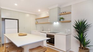A modern kitchen with white cabinetry, a central island, and wooden stools. - Tumut Unit 2- Easy Walk to Rainbow Bay Beach and Twin Towns Services club, Wi-Fi is included (Tweed Heads)