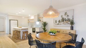 A modern kitchen with white cabinets, a central island with stools, a dining table with chairs, and a hanging light fixture. - Tumut Unit 2- Easy Walk to Rainbow Bay Beach and Twin Towns Services club, Wi-Fi is included (Tweed Heads)