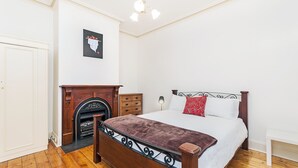 A bedroom with a wooden bed, a fireplace, a nightstand, and a wall-mounted picture. - Positioned in the center of Warrnambool at a location that cannot be beat. (WARRNAMBOOL)