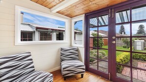 A room with a wooden ceiling, a large window, and a door leading outside. There are two zebra-patterned chairs and a small table. - Positioned in the center of Warrnambool at a location that cannot be beat. (WARRNAMBOOL)