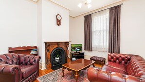 A living room with leather sofas, a wooden coffee table, a fireplace, a television, and a clock on the wall. - Positioned in the center of Warrnambool at a location that cannot be beat. (WARRNAMBOOL)