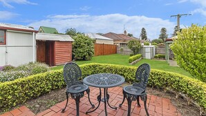 A patio with a table and chairs, surrounded by well-maintained hedges and a lawn. - Positioned in the center of Warrnambool at a location that cannot be beat. (WARRNAMBOOL)