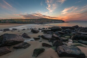 A beach with large rocks and a forested hill in the background.
