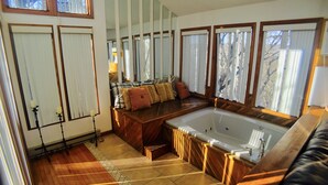 Une salle de bain moderne avec une grande baignoire, un plancher en bois et un coin salon agrémenté de coussins.