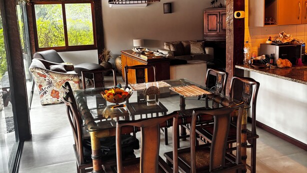 Un espace repas comprenant une table et des chaises en bois, une table avec un plateau en verre, et une vue sur l’extérieur grâce à une grande fenêtre.