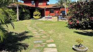 Une maison rouge à deux étages, avec un toit en tuiles, entourée de palmiers et un chemin de pierre menant à l’entrée.