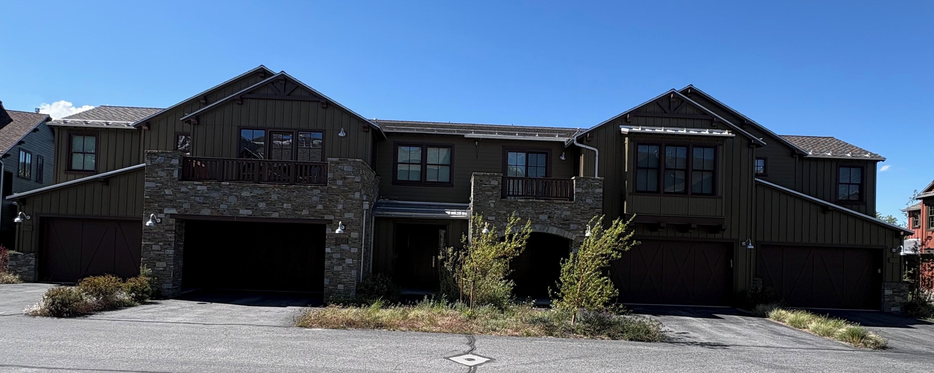 A two-story house with a stone facade, multiple garage doors, and a clear blue sky.