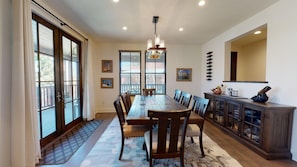 A dining area with a long wooden table, chairs, a chandelier, and a cabinet with bottles.