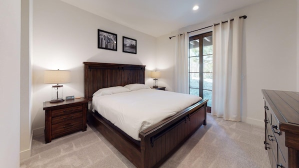 Un dormitorio con una cama grande, dos mesitas de noche con lámparas, un cabecero de madera y una ventana con cortinas.