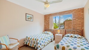 A bedroom with two single beds, a wooden chair, a nightstand, a ceiling fan, and a window with a view of the outside.