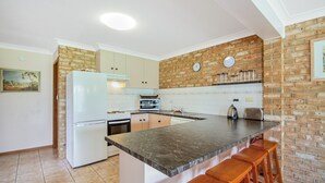 A kitchen with a brick wall, a refrigerator, a stove, a microwave, and a sink.