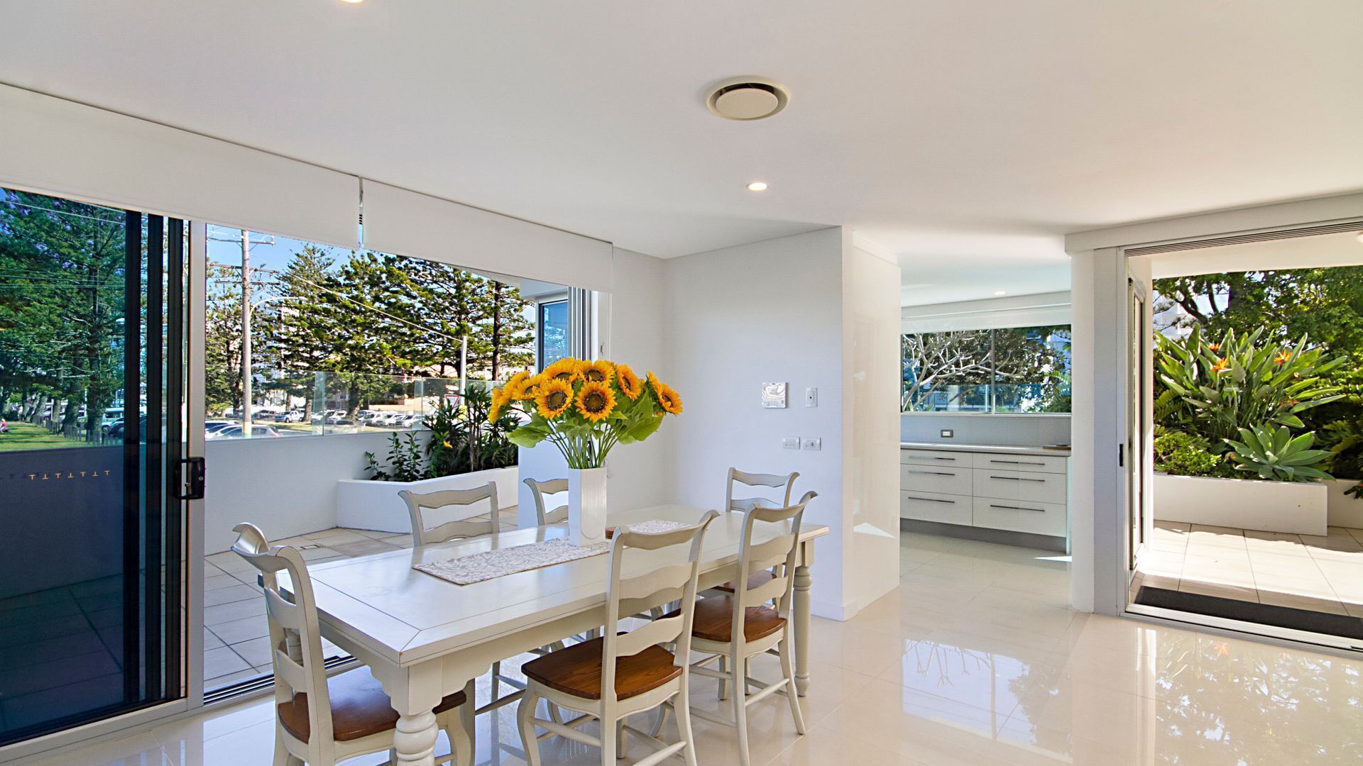 A modern dining area with a white table, four chairs, and a vase of sunflowers.