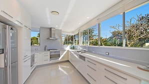 Una cocina moderna con armarios blancos, electrodomésticos de acero inoxidable y ventanas amplias con vistas al exterior.
