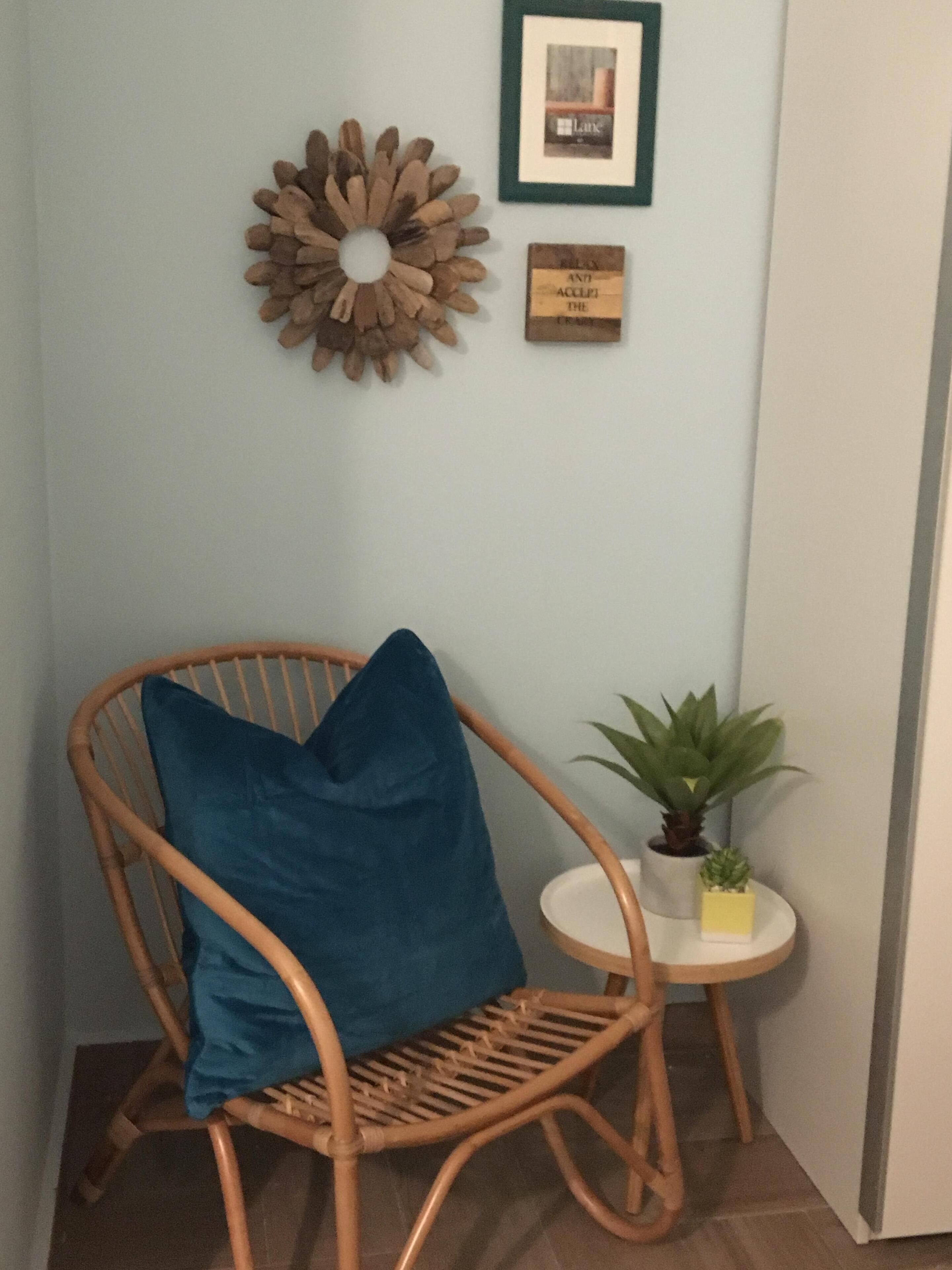 Un racó amb una cadira de fusta, una taula rodona petita amb una planta, i una paret amb una decoració de fusta i un quadre amb marc.