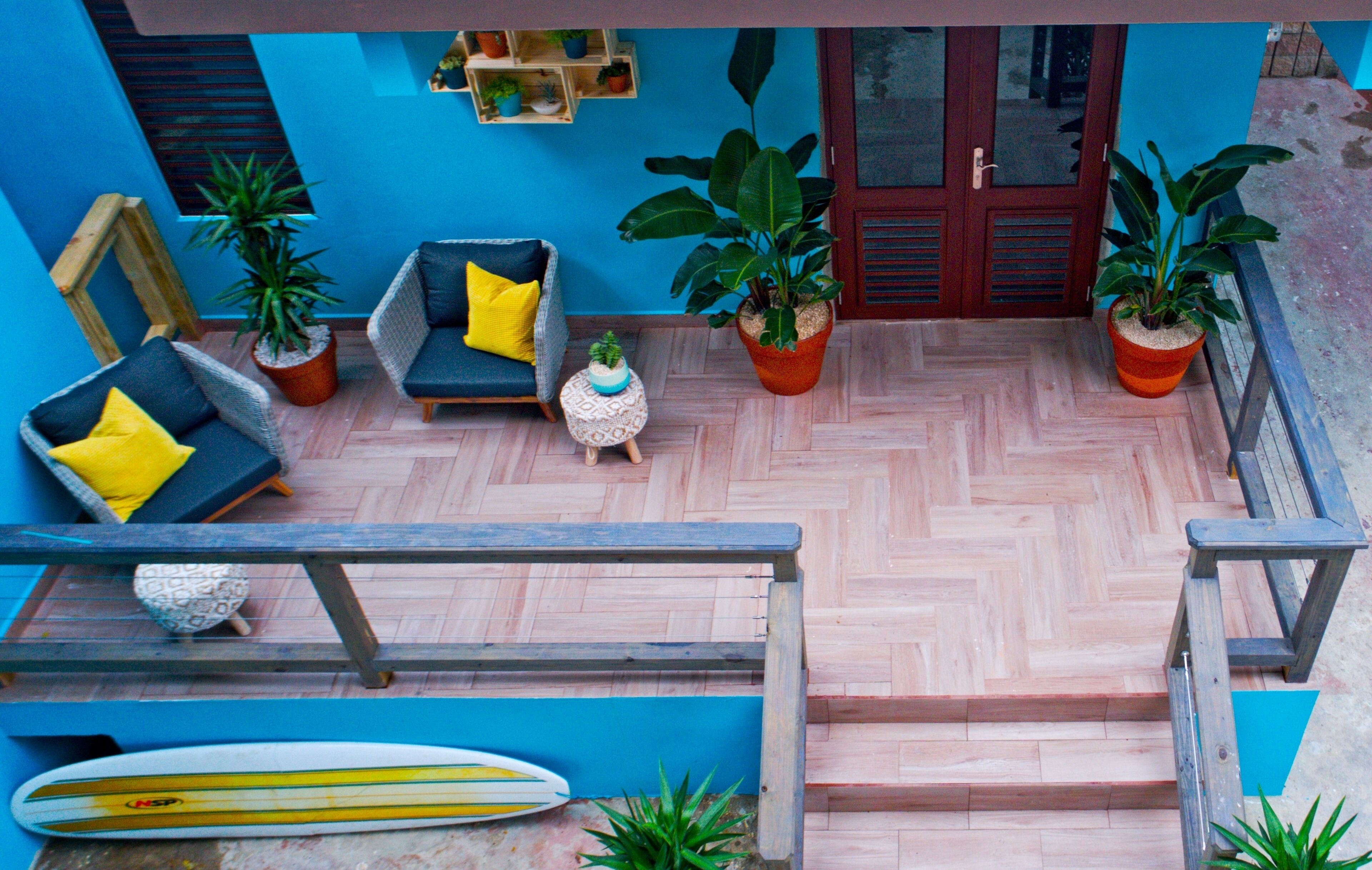 A patio with a blue wall, a wooden bench, a surfboard, and potted plants.