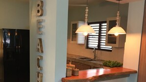 A kitchen with a wooden countertop, two stools, a refrigerator, and a wall-mounted light fixture. - Cocoloba #2 at Crash Boat - A Unique Beach Front Experience (Aguadilla)