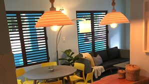 A dining area with a round table, yellow chairs, and a wooden bench. There are two pendant lights hanging above the table. - Cocoloba #2 at Crash Boat - A Unique Beach Front Experience (Aguadilla)