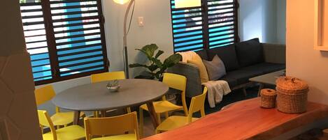 A dining area with a round table, yellow chairs, and a wooden bench. There are two pendant lights hanging above the table.