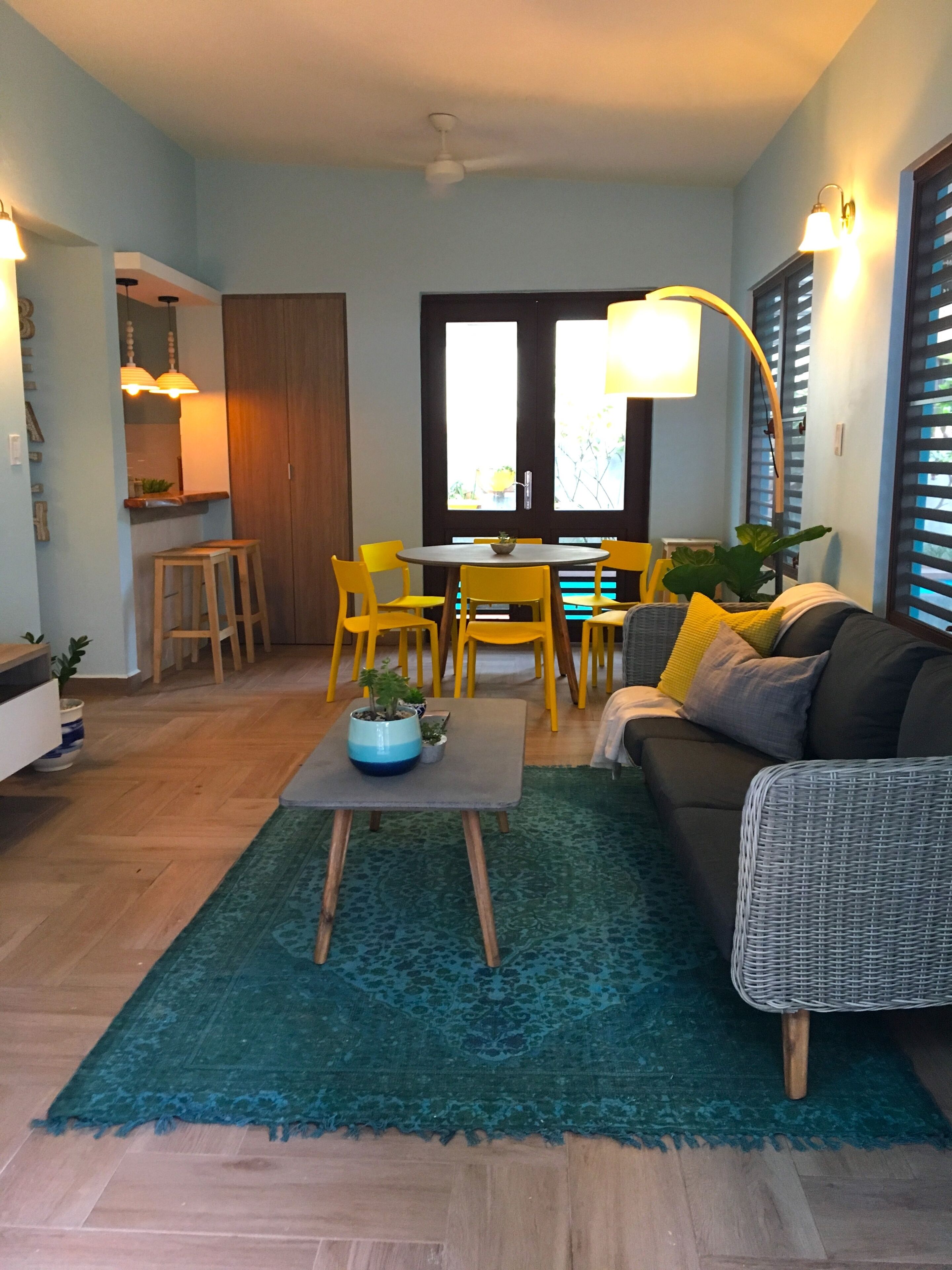A modern living room with a dining area, featuring a sofa, chairs, a coffee table, and a kitchen in the background.