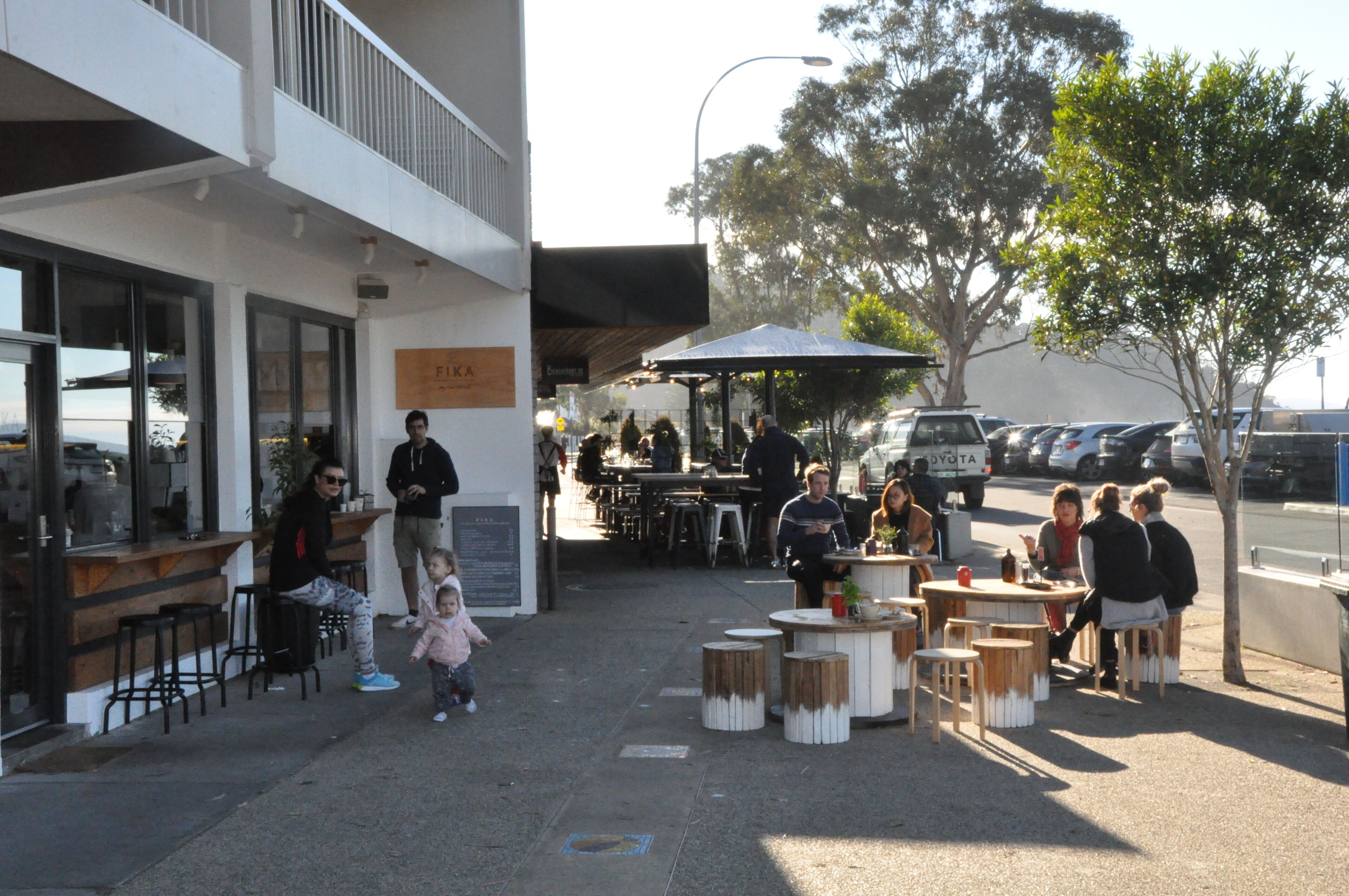Un café en plein air avec des tables et des chaises, un espace de repos abrité et une enseigne indiquant un restaurant.